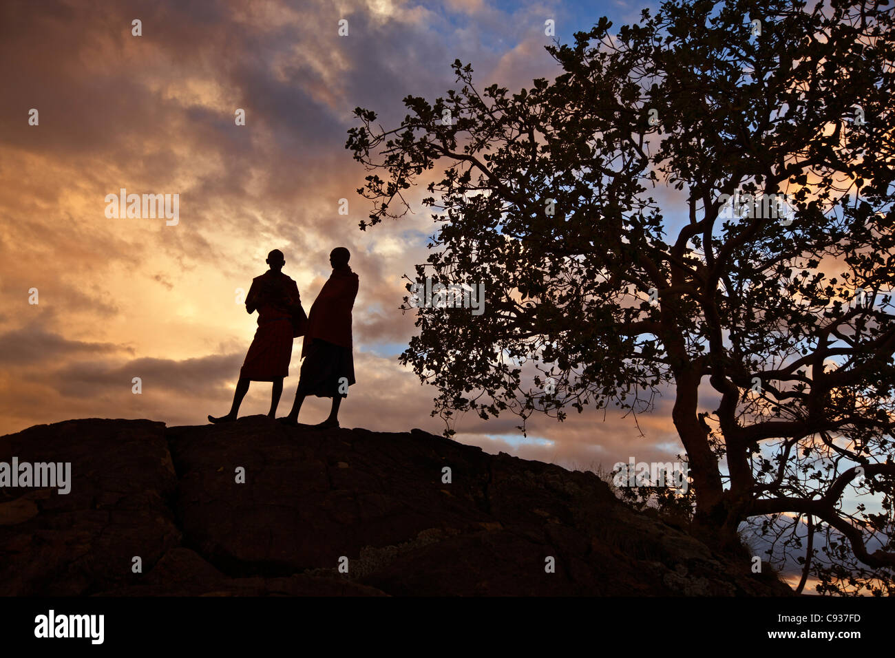 Two Maasai men silhouetted on a hill at sunset. Stock Photo