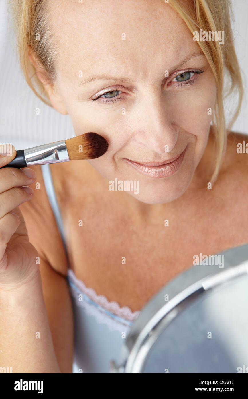 Mid age woman putting on make-up Stock Photo