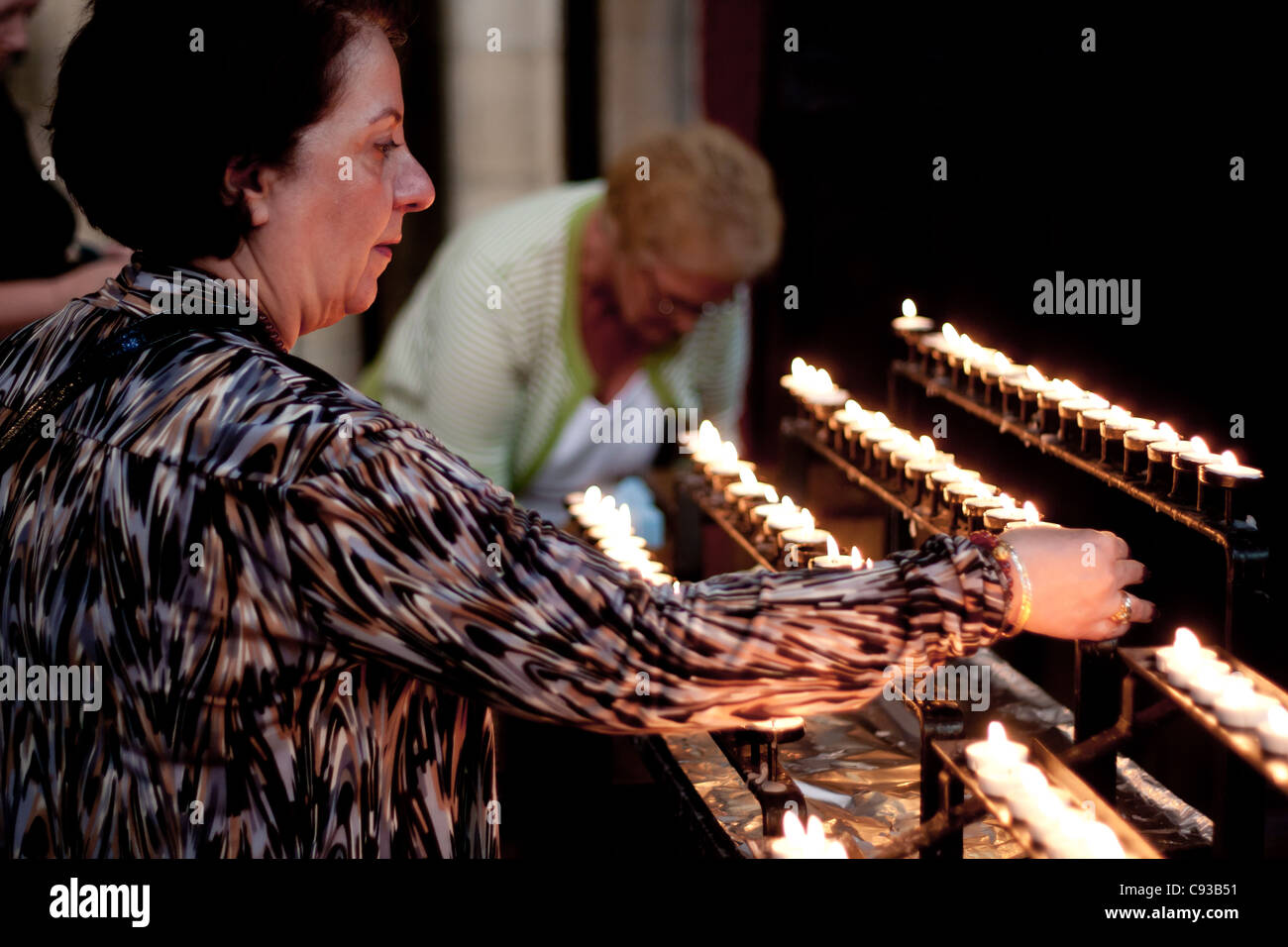 A lady lighting a candle in prayer within a church cathedral before God