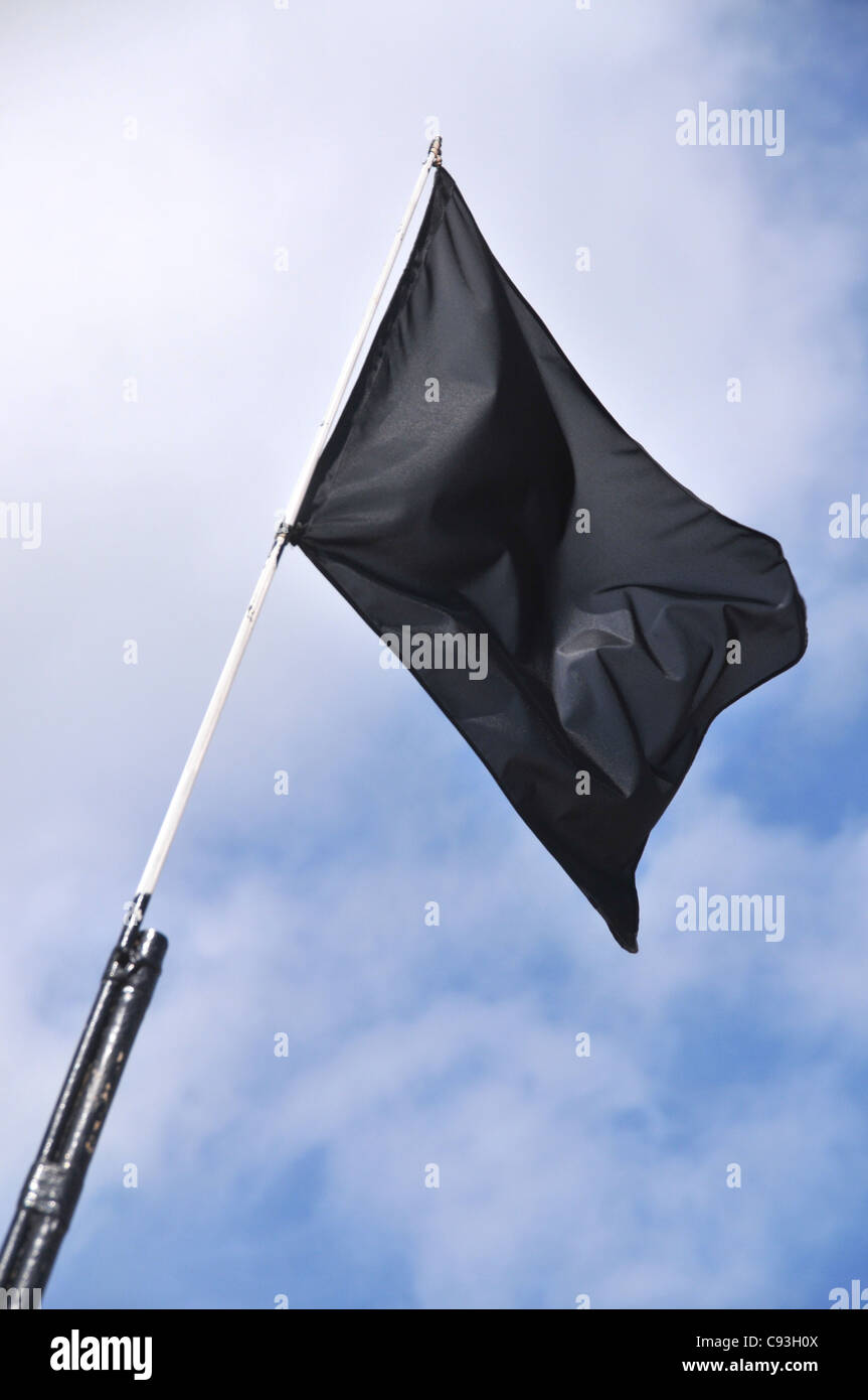 A blank black flag flying in the wind against a cloudy blue sky. Stock Photo