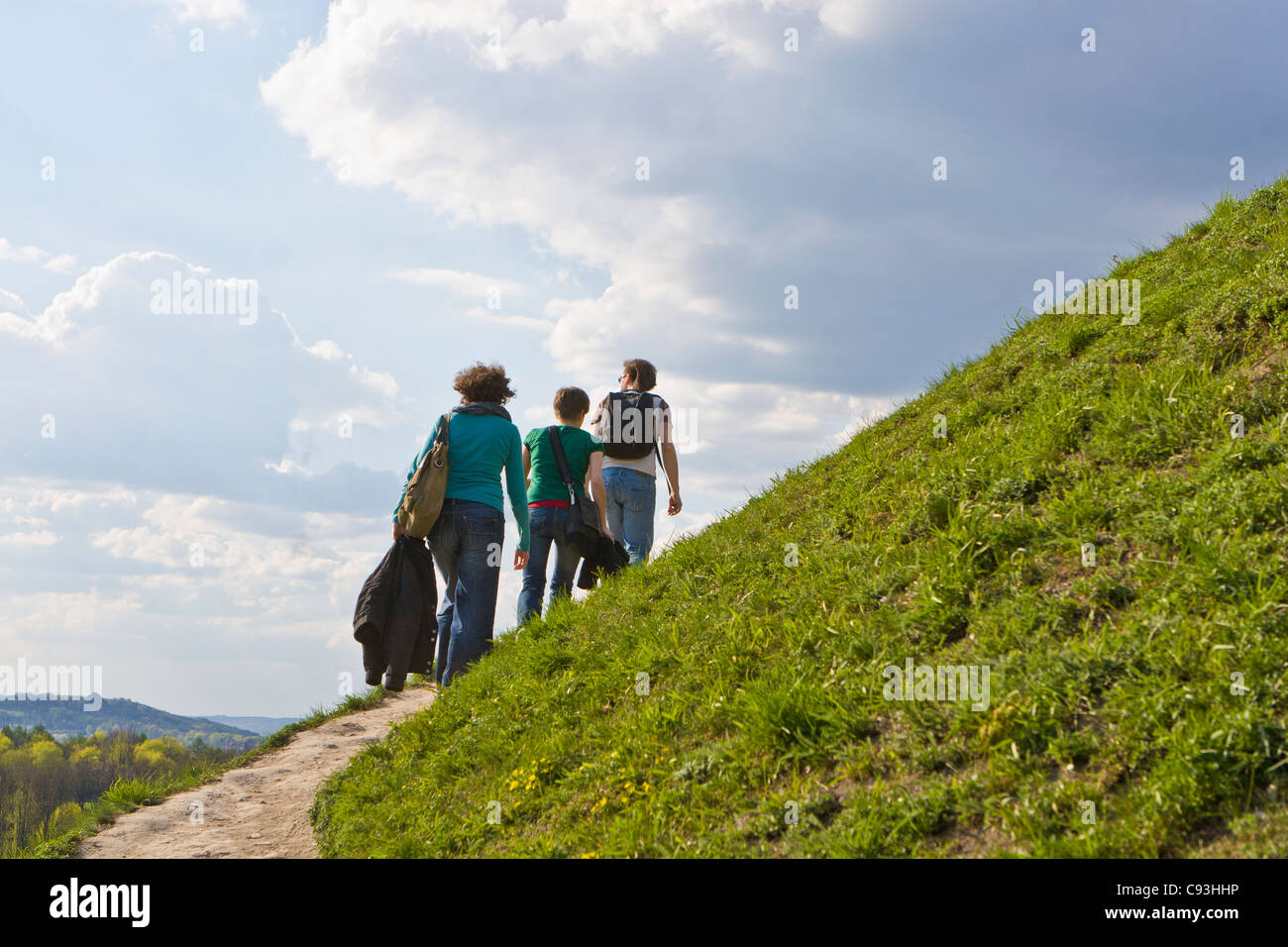 Three young people climb a grassy hill Stock Photo