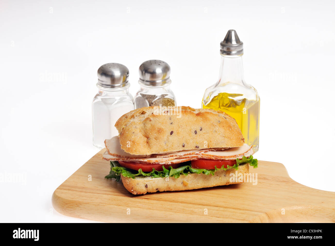 Chicken with lettuce and tomato sandwich in a roll on wood chopping board with condiments of salt, pepper and olive oil on white Stock Photo