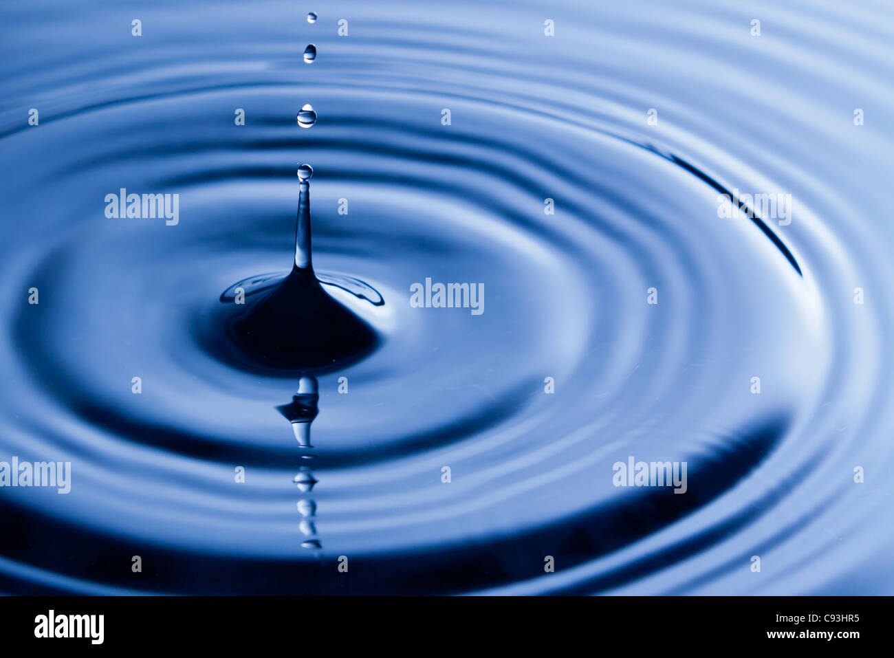 Water droplet bouncing up out of a pool of rippling blue water creating ...