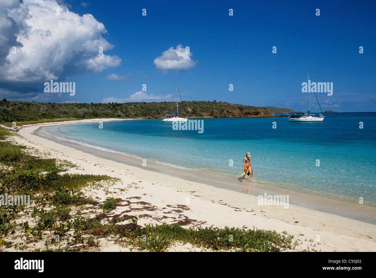 Woman with snorkeling gear walking on beach and yachts anchored in bay at Bahia des Tortugas; Culebra Island, Puerto Rico. Stock Photo