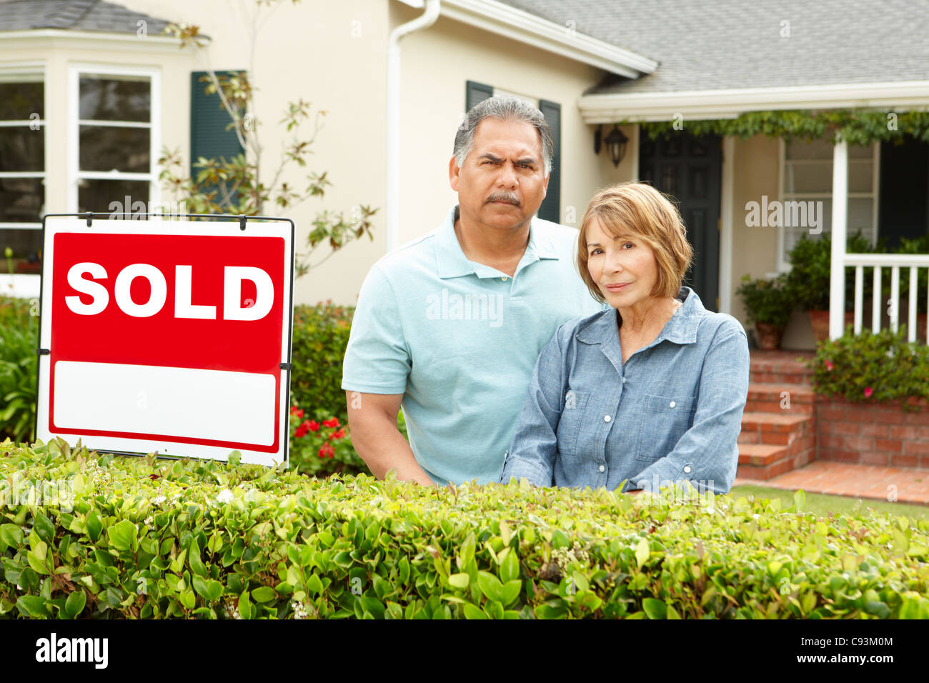 Senior Hispanic couple outside house with sold sign Stock Photo