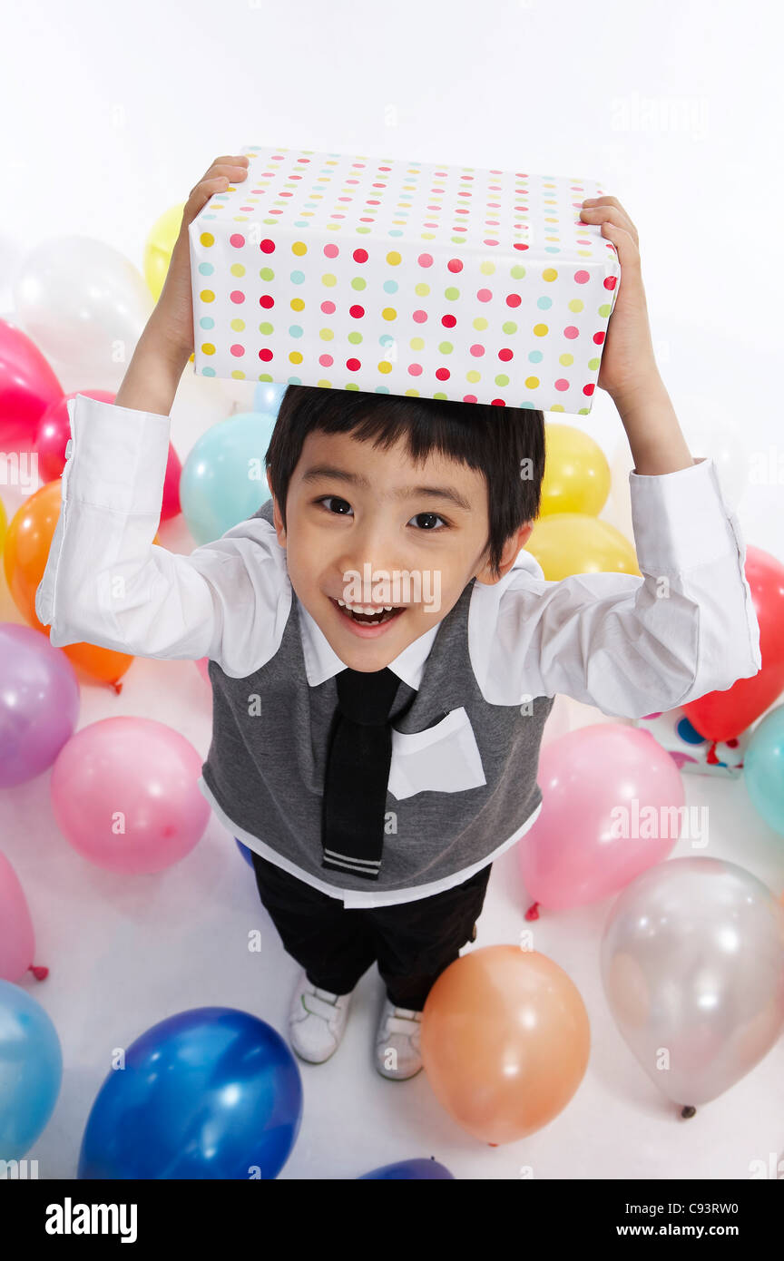 Portrait of boy standing between balloons with holding gift box over ...