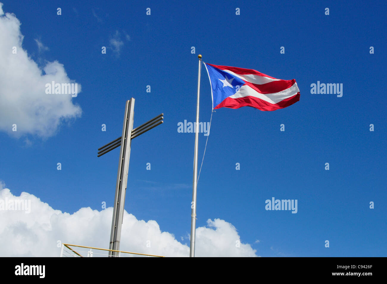 Picture shows a flag of Puerto Rico fluttering in the sun and a cross side by side symbolizing the Catholic faith of the people. Stock Photo