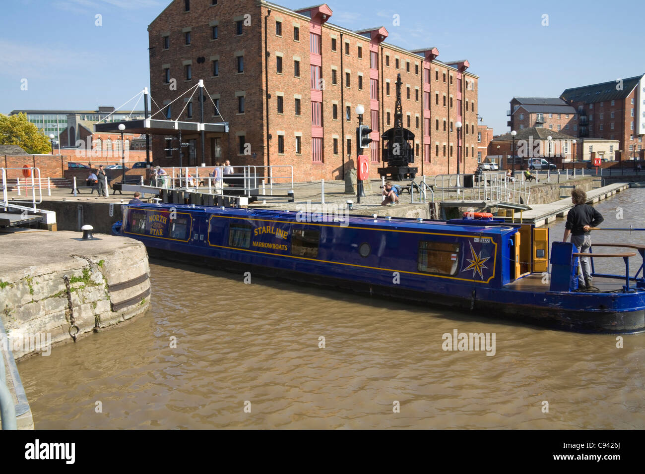 Gloucester England Helmsman steering blue narrowboat from Dock Basin into lock by North Telford Warehouse Stock Photo