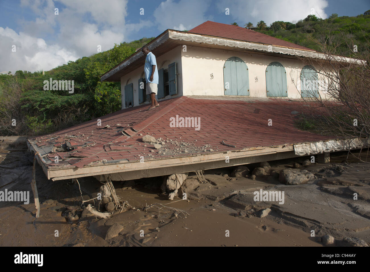 Man standing on the roof of the three storey Crowe House buried by mud flows, called lahars, down the Belham River, Montserrat Stock Photo