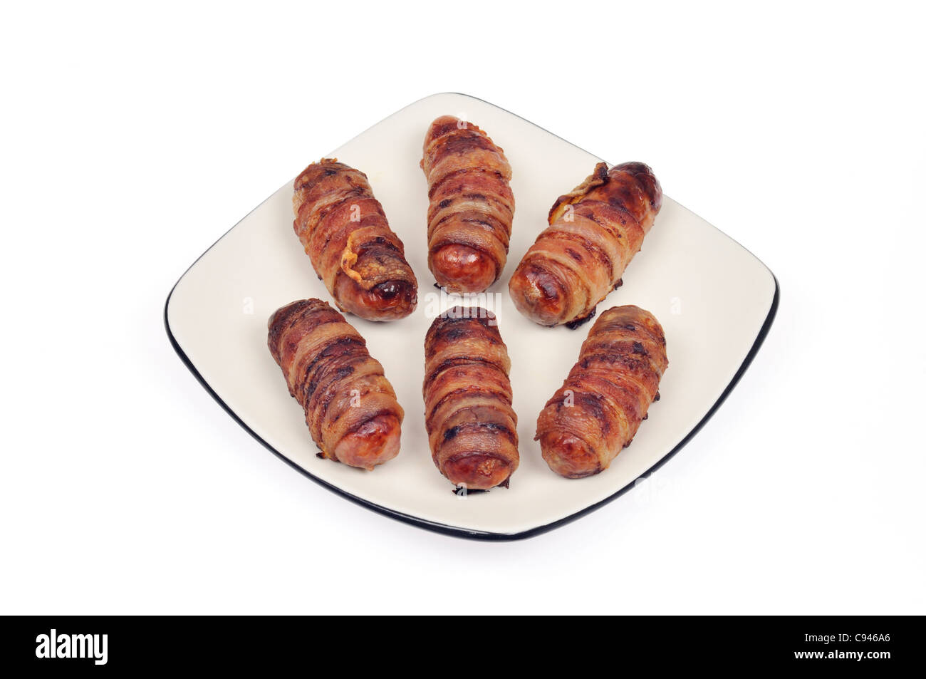 Cooked pigs in blankets sausages wrapped in bacon on white plate on white background cutout. Stock Photo