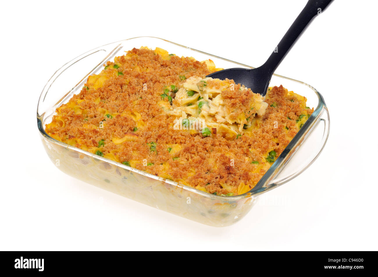 Close up of creamy baked tuna noodle cheese casserole with green peas topped with buttery breadcrumbs with serving spoon in pyrex on white background. Stock Photo
