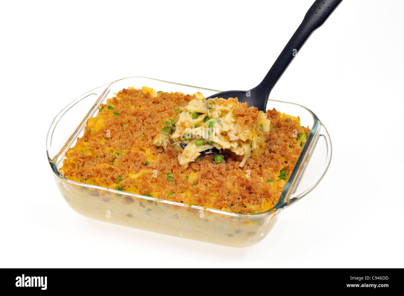 Close up of creamy baked tuna noodle cheese casserole with green peas topped with buttery breadcrumbs with serving spoon in pyrex on white background. Stock Photo