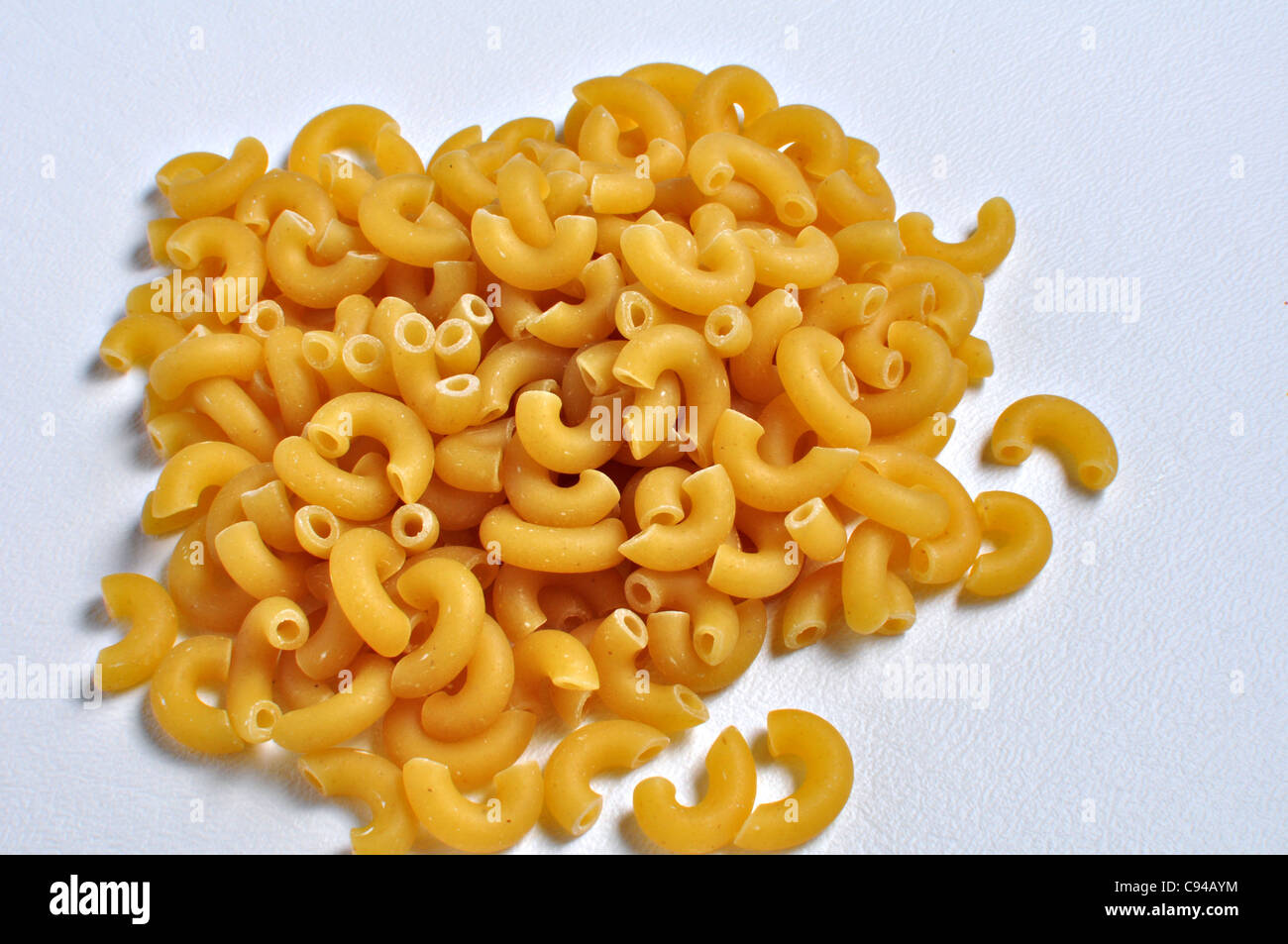 A pile of dry elbow macroni noodles sits on a white background Stock