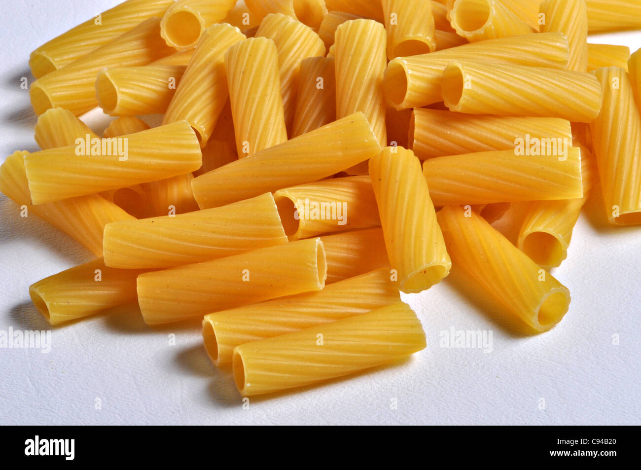 A pile of rigatoni pasta sits on a plain background. Stock Photo