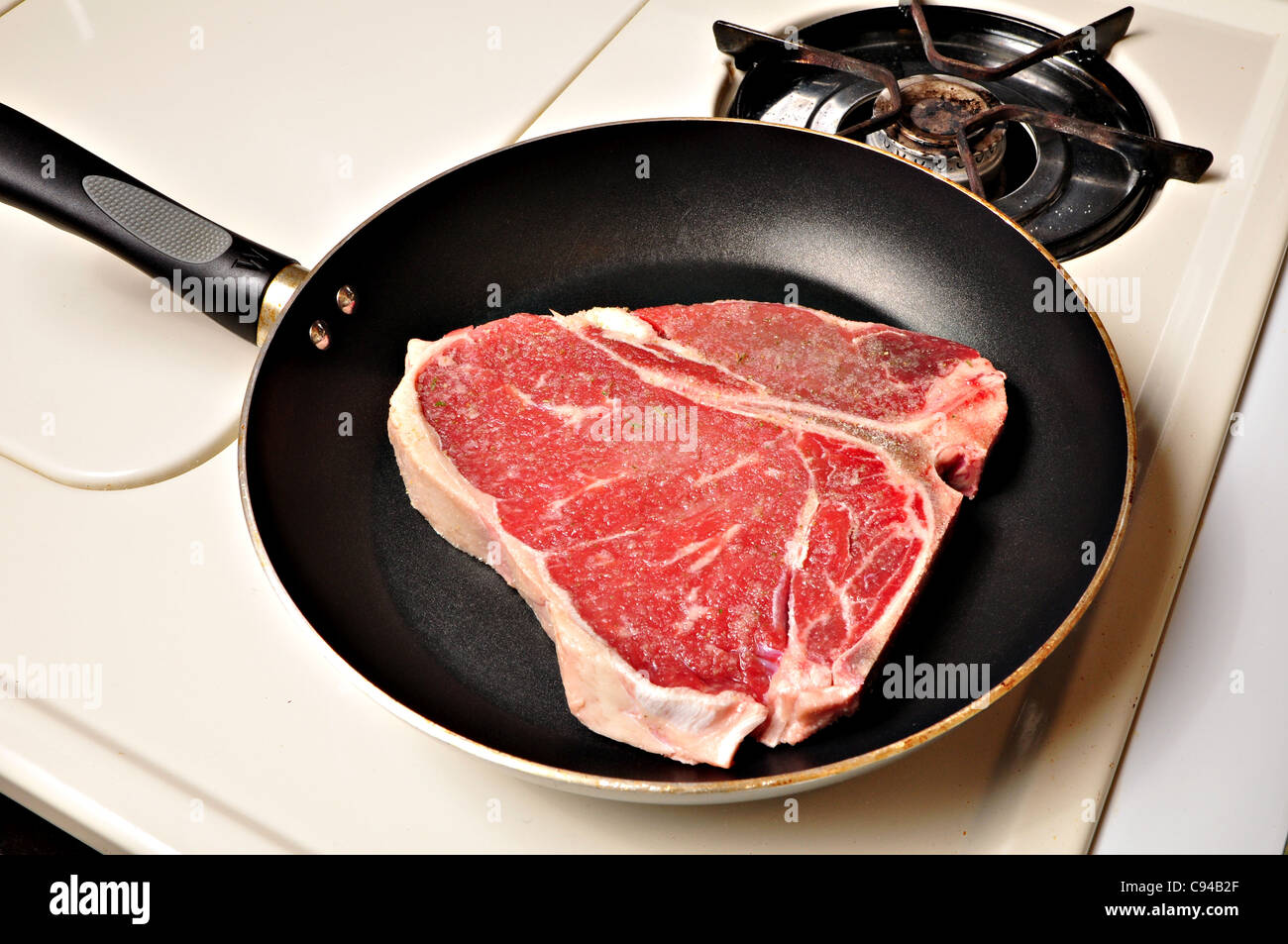 A tbone steak is being cooked on a stove in a frying pan Stock Photo