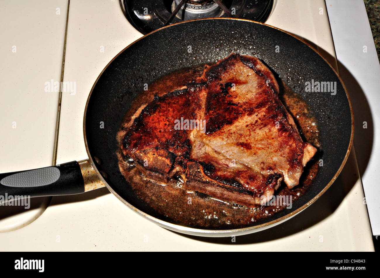 A t-bone steak is cooking in a frying pan. Stock Photo