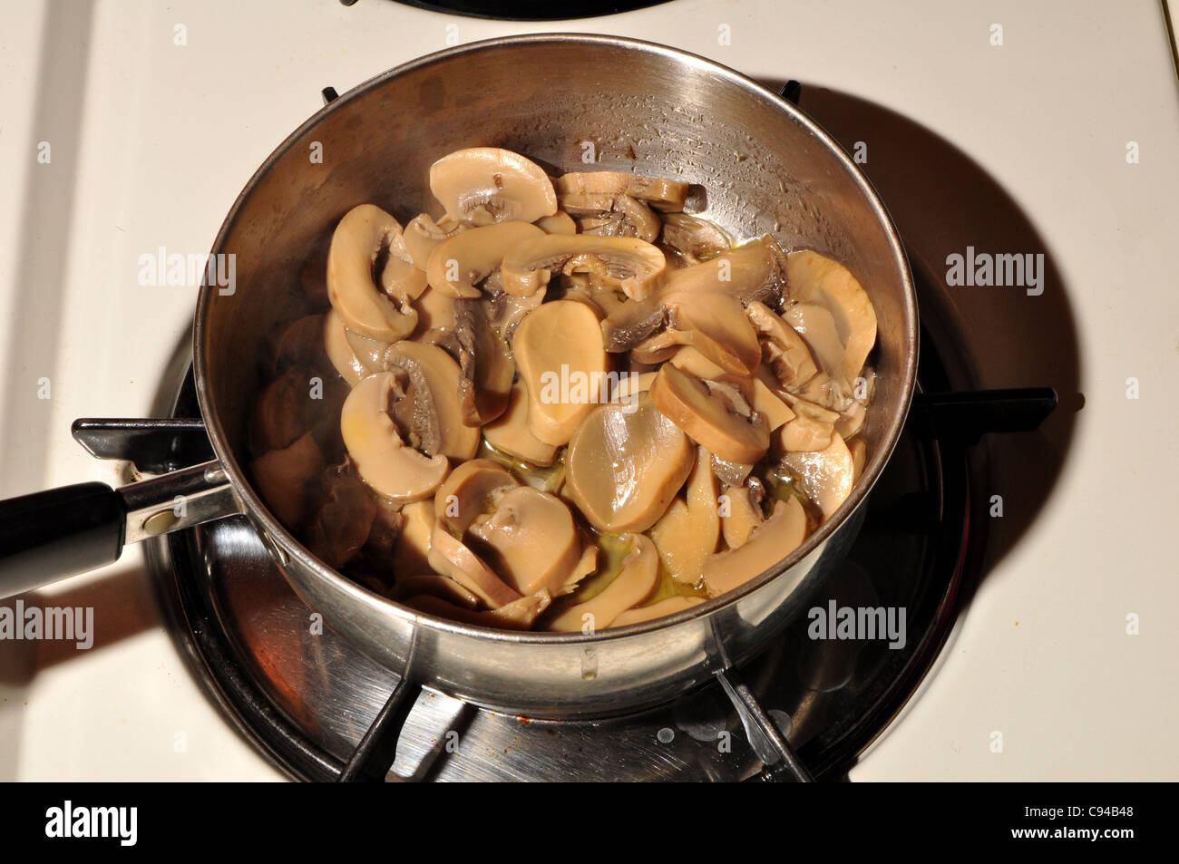 A pan of mushrooms cooking on a stove. Stock Photo