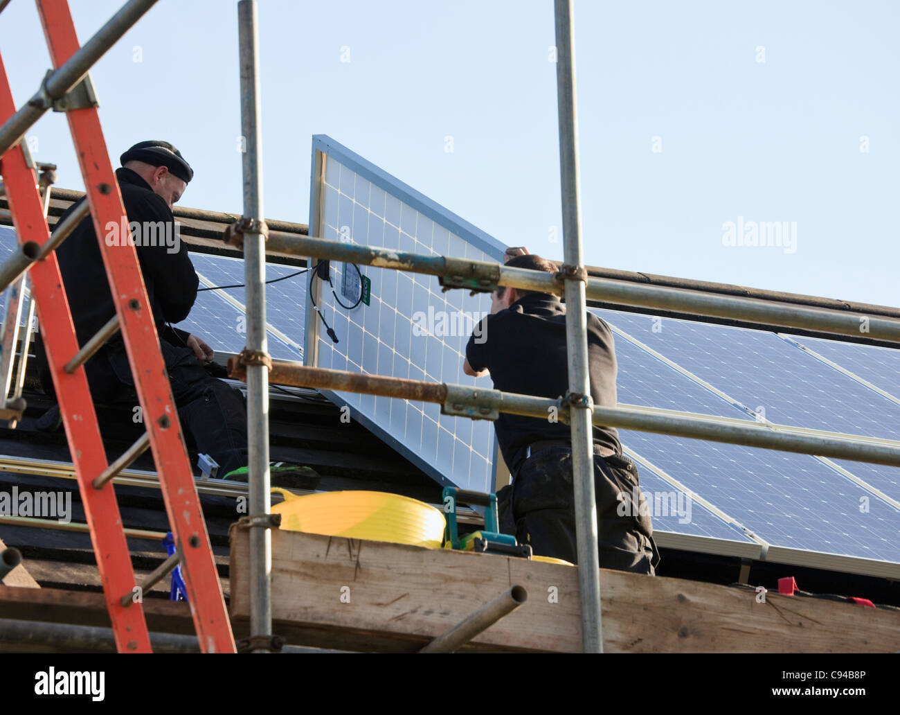 Workmen fitting new solar panels to a house roof for the Feed-in Tariff scheme. Wales, UK, Britain Stock Photo