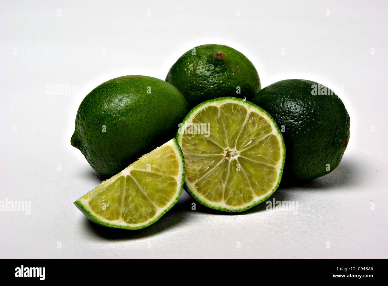 Limes and pieces of limes sit on a plain background. Stock Photo