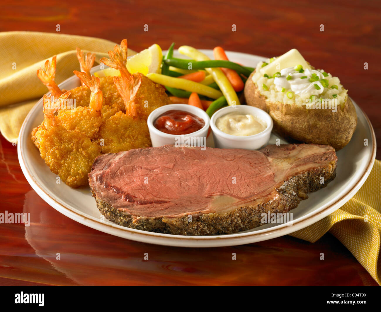 Prime rib and shrimp dinner with loaded stuffed potato and vegetable Stock Photo