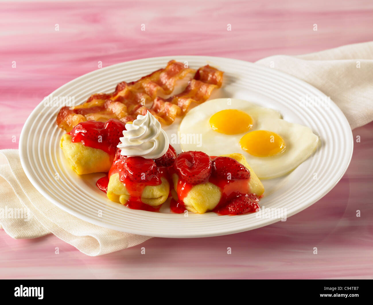 Breakfast cheese crepe blintz with fruit sauce topped with whip cream with two eggs and bacon Stock Photo