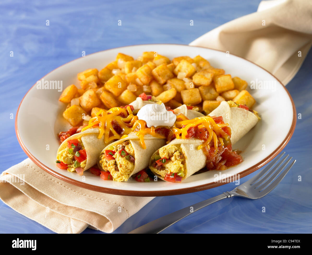 Breakfast enchiladas stuffed with egg and topped with salsa, cheese and sour cream and served with potato Stock Photo