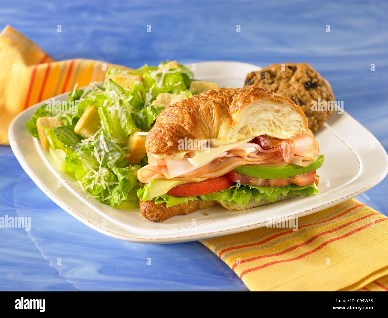 Gourmet croissant club sandwich with turkey, swiss cheese, lettuce, tomato avocado and served