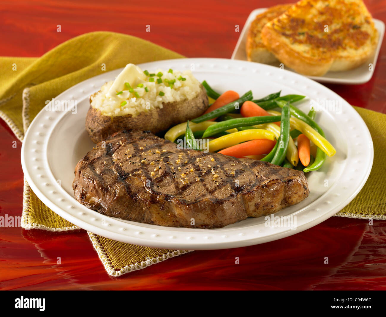 Rib eye steak served with a loaded baked potato, vegetables and garlic bread Stock Photo
