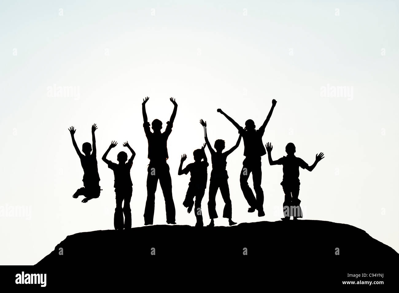 Silhouette of young Indian boys jumping on a rock against the sun / light sky Stock Photo