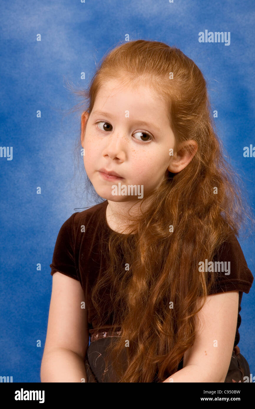 Red-haired elementary school age girl with long hair sitting with very calm and thoughtful facial expression Stock Photo