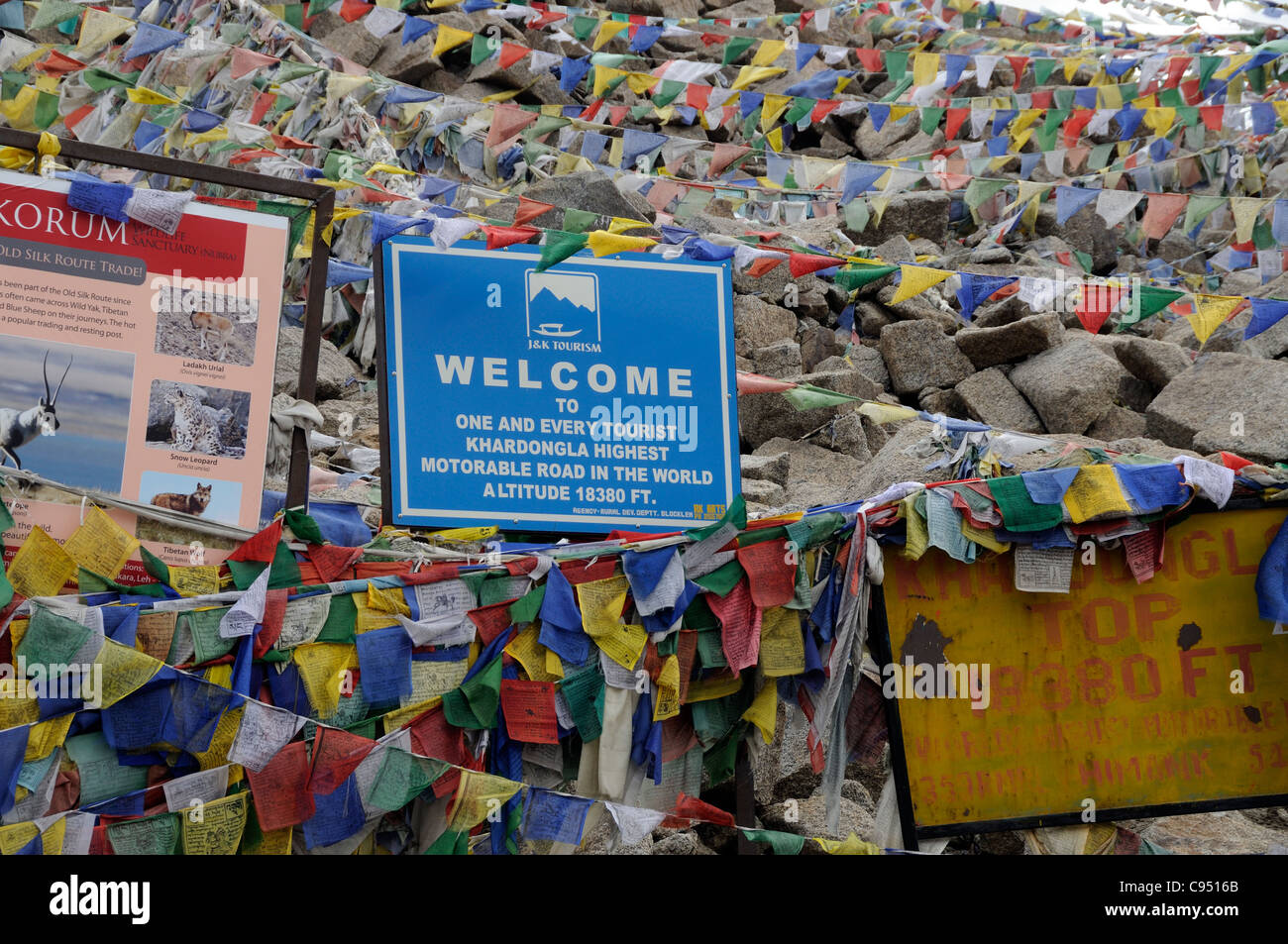 Prayer flags and signs at the top of what claims to be the world's highest drivable road pass, Khardung La. Stock Photo