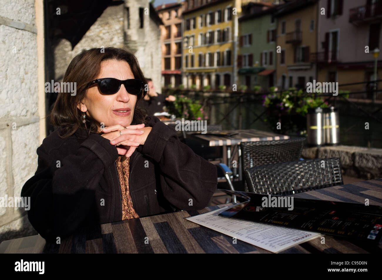 Woman with sun glasses in outdoor coffee shop by the Thiou River. Annecy, France. 20/09/2011. Stock Photo