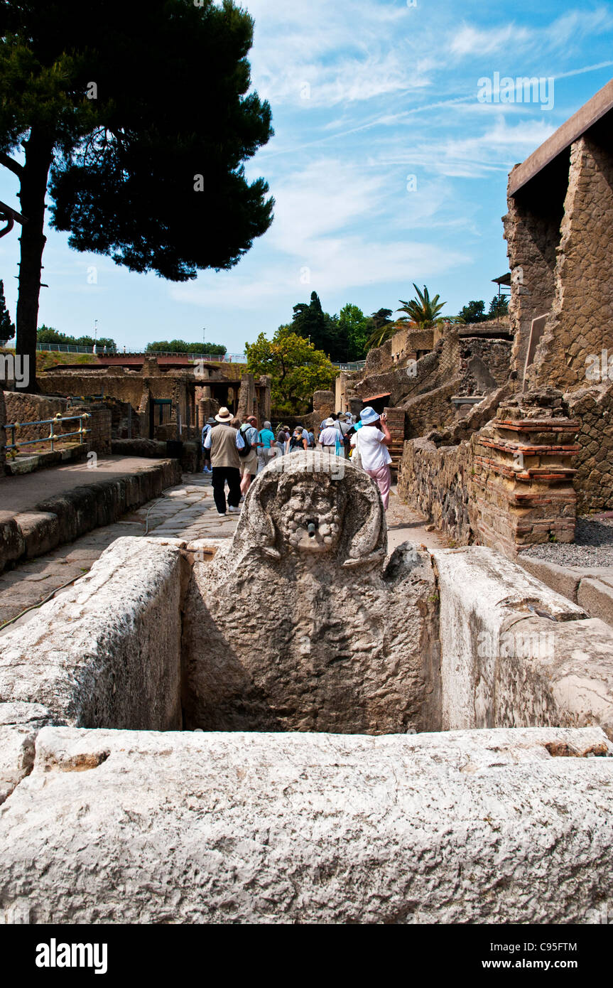 A public fountain with a sculptured headstone over a rectangular stone trough situated at a street intersection in Herculaneum Stock Photo