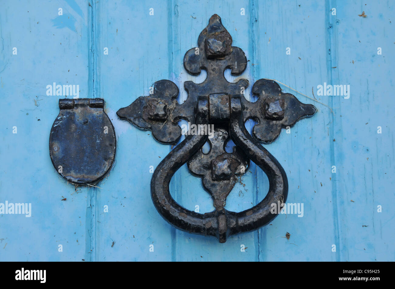 A blue wooden door with an ornate and old  door handle and knocker with keyhole and cover. Stock Photo