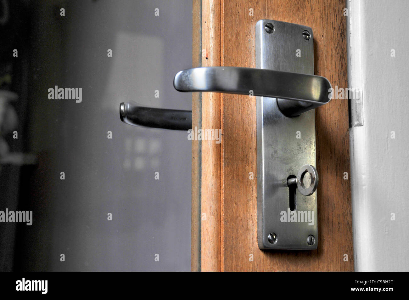 A locked glass door and door handle with a key in the keyhole. Stock Photo