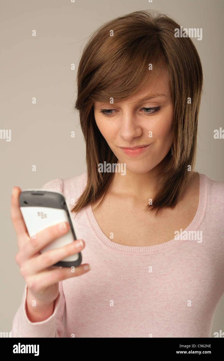 Pretty teenage girl holding a smartphone and looking suspicious. Stock Photo