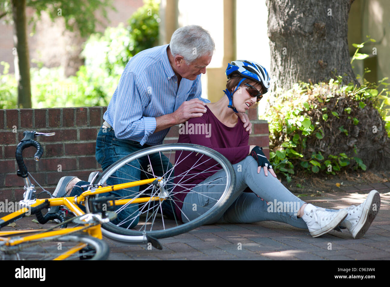 Cycling accident. Man helping a cyclist that has fallen from her bike. Stock Photo