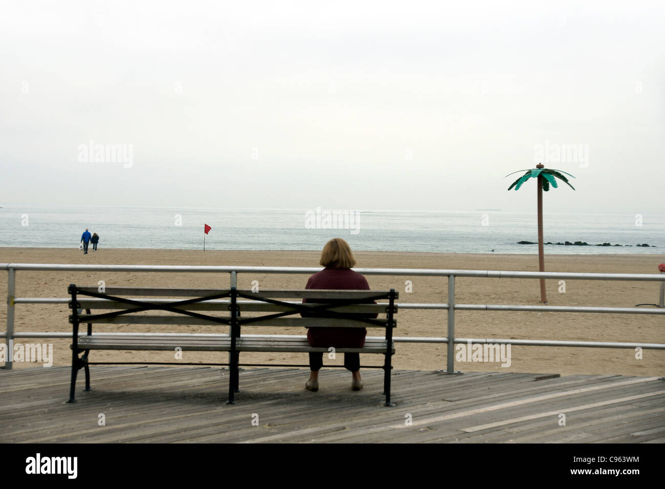 A solitary woman sits on a bench on the Broadwalk, Brighton Beach, New York CIty, New York, USA. (c) Marc Jackson Stock Photo