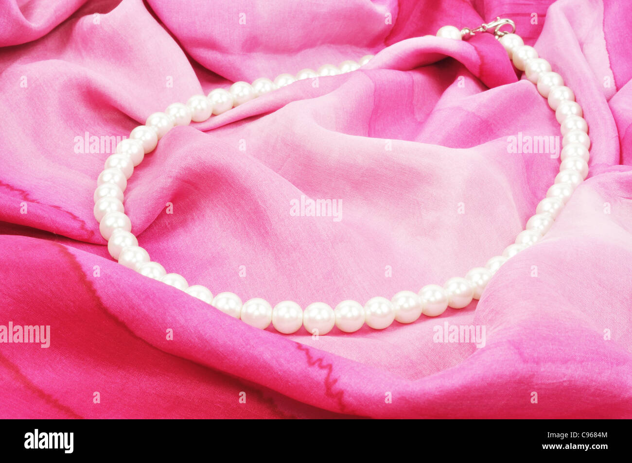 White pearl necklace laying on pink silk, close up Stock Photo