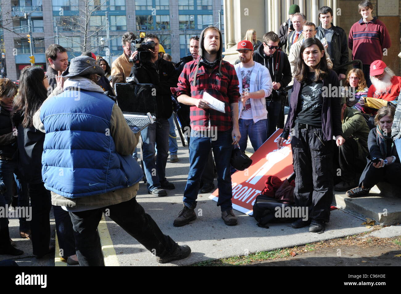 November 15, 2011, a group of Occupy Toronto protesters hold a noon hour general assembly in front of St. James Church to discuss their options following the delivery of an eviction notice, requiring the protesters to vacate St. James Park as of 12:01am, November 16, 2011. Stock Photo