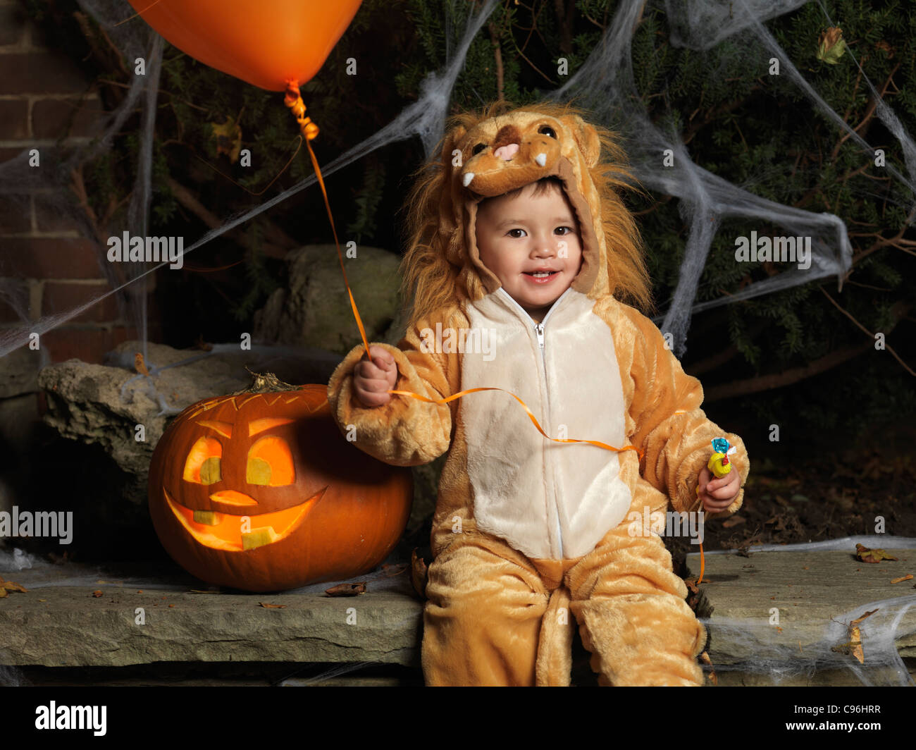 License available at MaximImages.com - Baby boy in a Halloween costume with a balloon and candy sitting beside a carved pumpkin Stock Photo