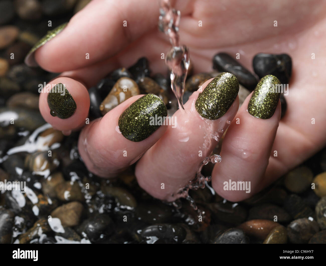 License available at MaximImages.com Closeup of woman hand with green fancy nail polish in water on pebble stones Stock Photo
