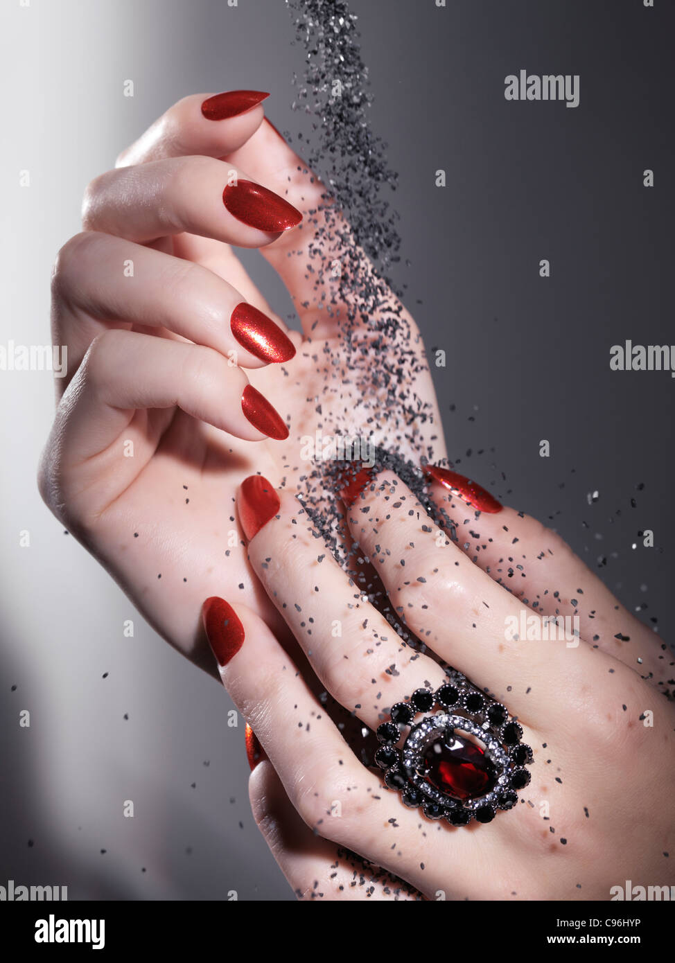 License available at MaximImages.com Black sand falling on woman's hands with bright red nail polish and a red stone ring Stock Photo