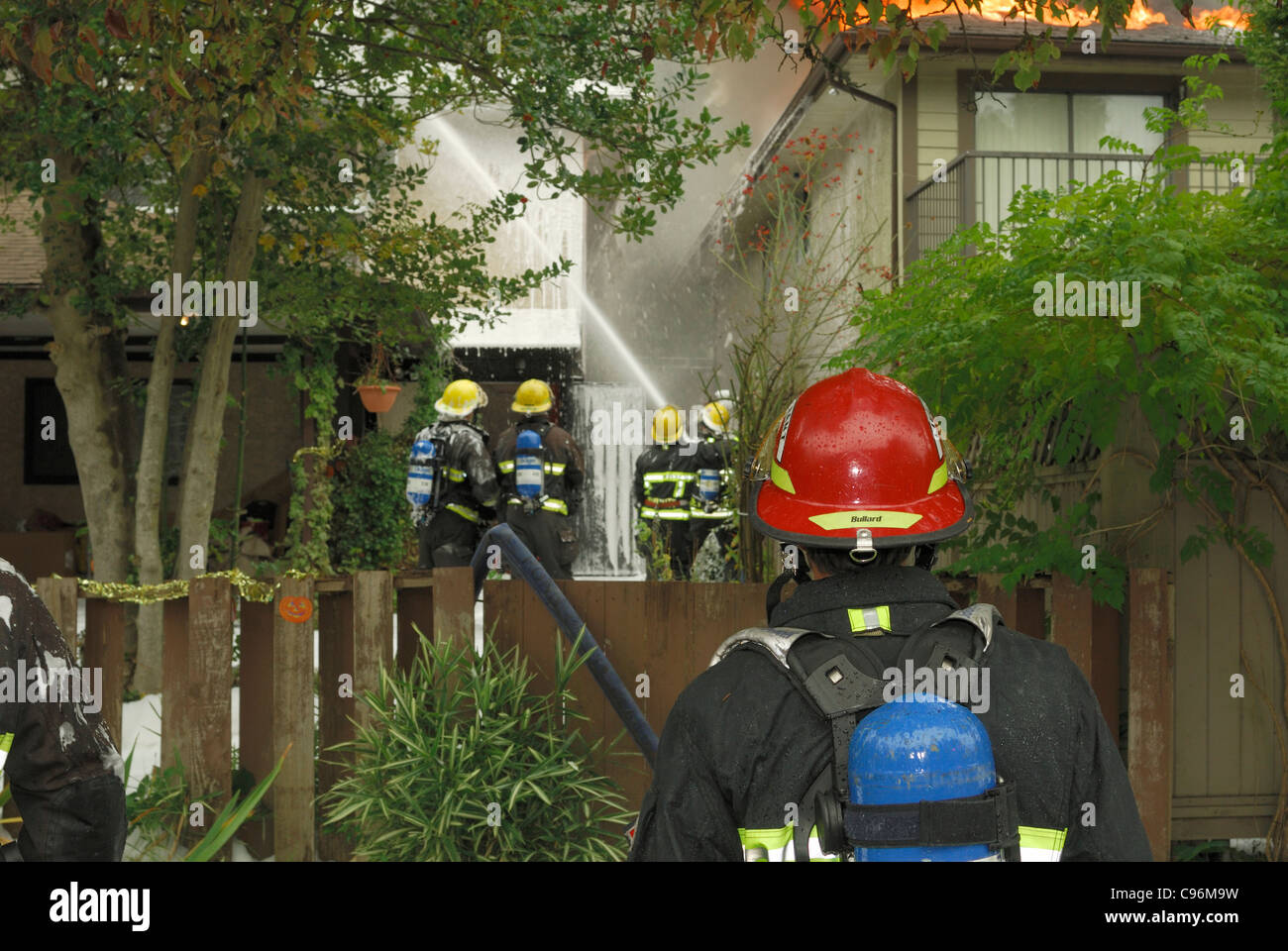 Vancouver fire lieutenant observing his men hosing a house with CAFS compressed air foam system to  prevent it from burning. Stock Photo