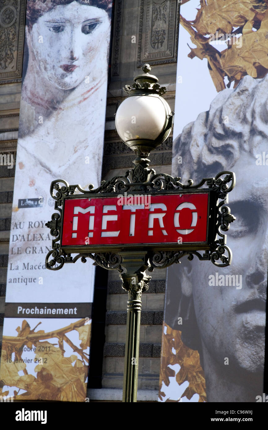 Art Nouveau Metro sign at the Louvre metro station with posters of Louvre exhibition on Louvre building Stock Photo