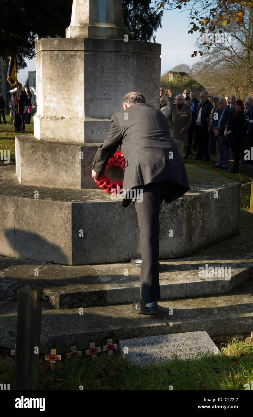 Man laying remembrance day poppy wreath on a war memorial in the grounds of St Lawrence church Abbots Langley Herts UK Stock Photo