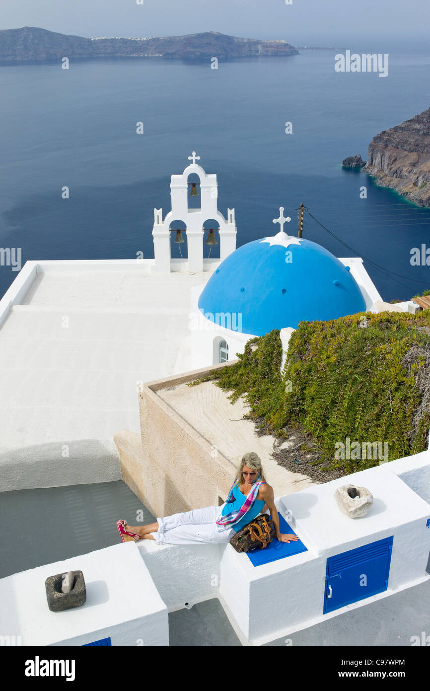 Woman relaxing on a wall above the Greek Orthodox church with a blue dome, Fira, Santorini, Greece, Europe Stock Photo
