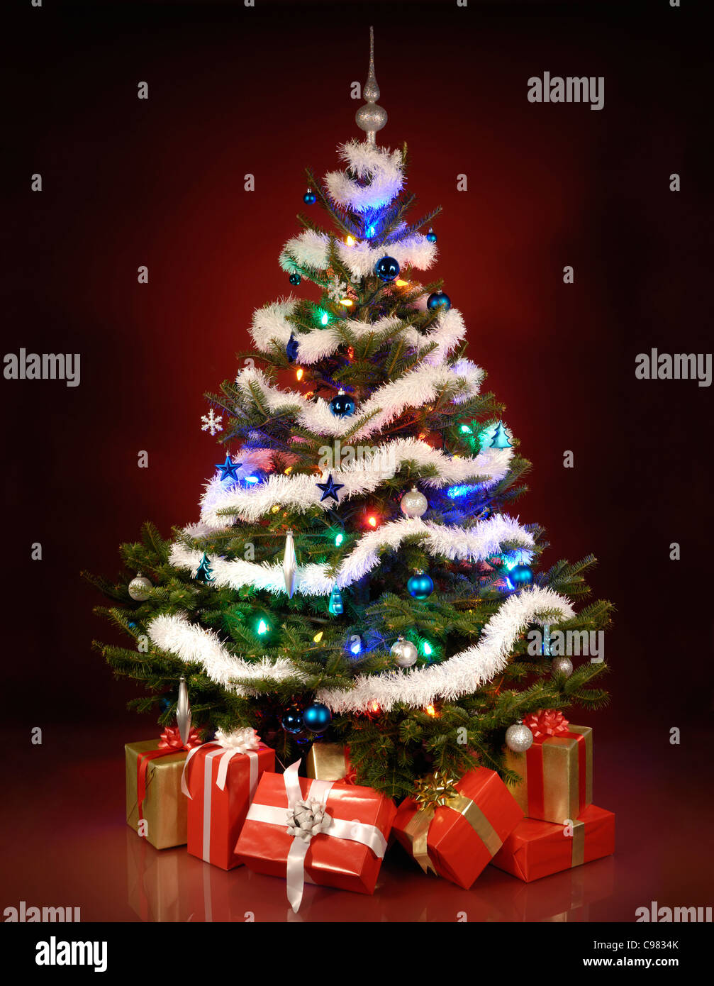 Shining decorated Christmas tree with gifts under it. Isolated on dark red background. Stock Photo