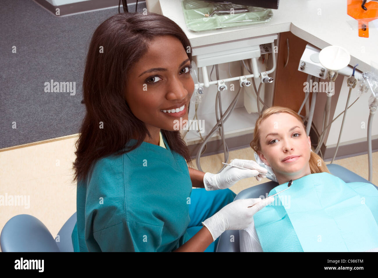Young Caucasian female opening mouth. African-American ethnic dentist in white latex gloves check her teeth (focus on dentist) Stock Photo