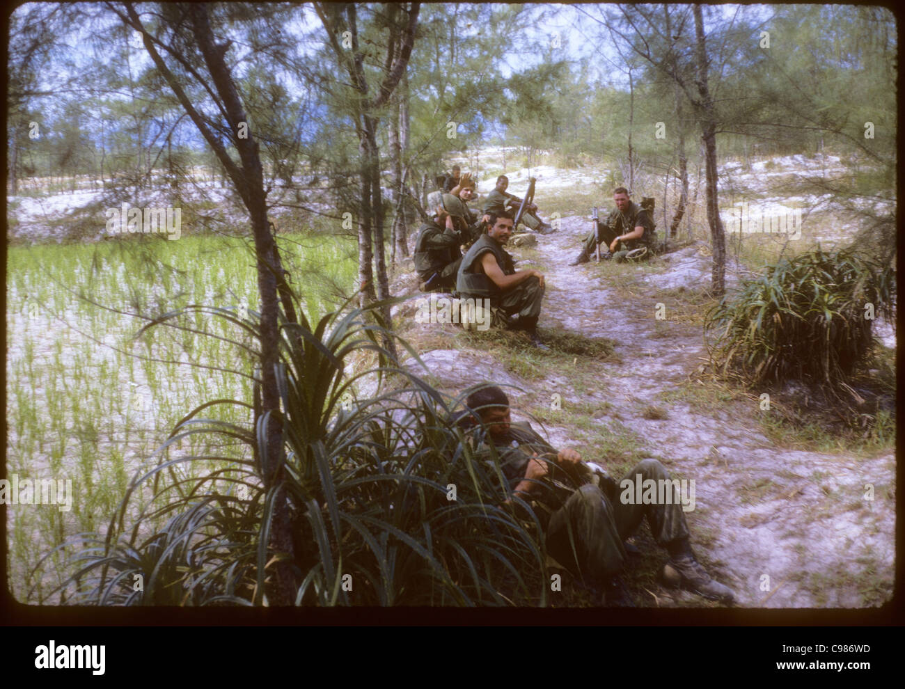 US GIs soldiers taking a rest during vietnam war infantry resting rice paddy sitting m-16 rifles trail agriculture nam break Stock Photo